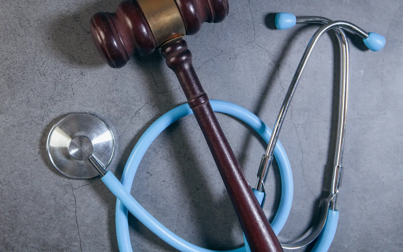 A wooden gavel resting across the coiled tubing of a stethoscope on a concrete surface